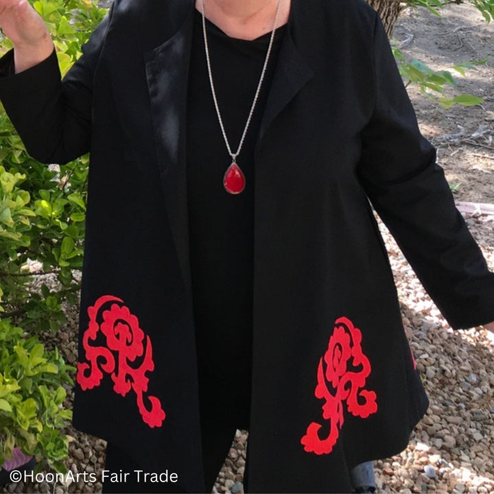 Closeup of black swing jacket, front view, showing large red hand-embroidered Suzan patterns at bottom front