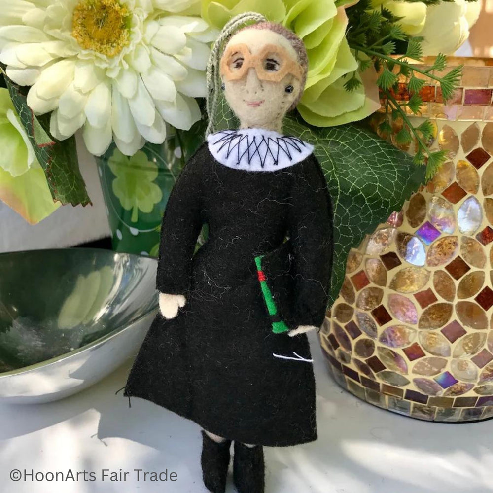 RBG Felt Ornament from Kyrgyzstan, Dressed in Black Judicial Robes and White Collar, Big Glasses, Carrying a Law Book, Against a Background of Flowers, a Silver Candy Dish and a Golden Mosaic Vase