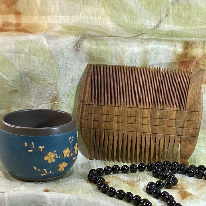 Double-side rectangular walnut comb with fine teeth on one side, wide teeth on the other, on green and white silk background with beads and cut in foreground