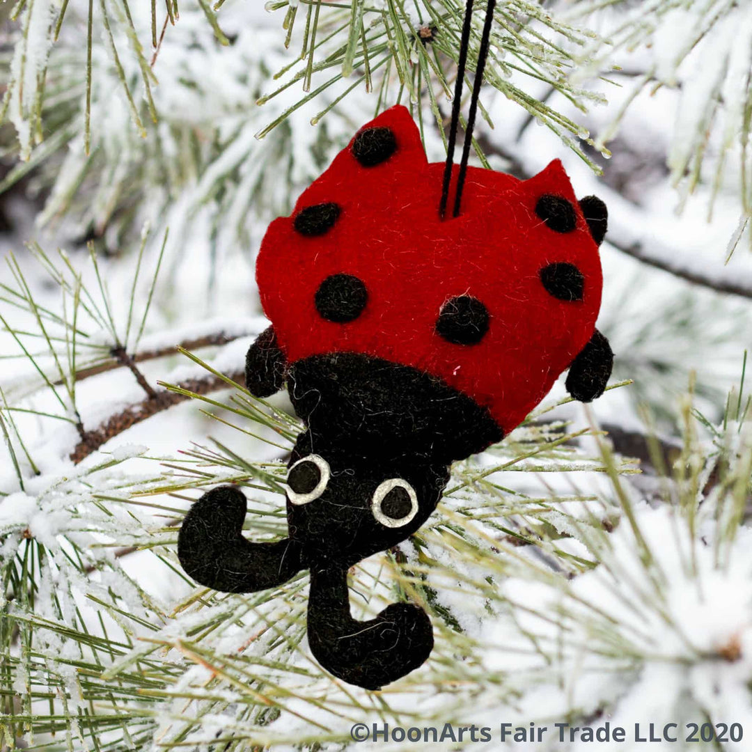 Red felt ladybug Christmas ornament, hanging from a snow-covered pine tree with long needles
