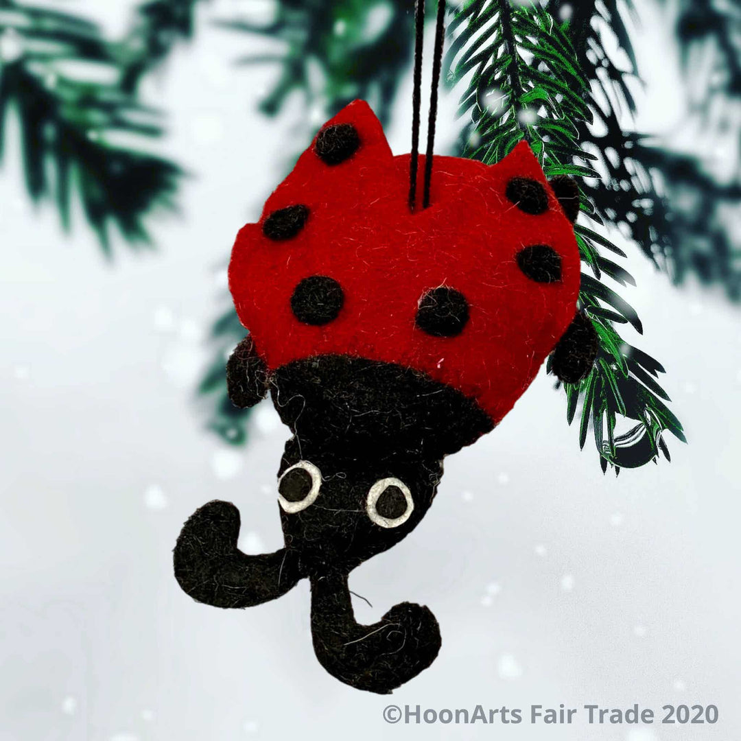 Bright red and black felt ladybug ornament, hanging from the tips of a pine Christmas tree