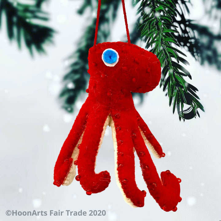 Handmade Felt Ornament-Red Octopus, with white underside, with red beads dotting the red upper side and bright blue eyes, hanging from a pine tree against a white background.