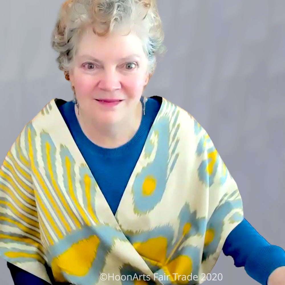 Handwoven silk ikat infinity shawl with traditional Uzbek pattern in blue and yellow on golden cream backgrounders, draped over the shoulders of older Caucasian woman in blue sweater