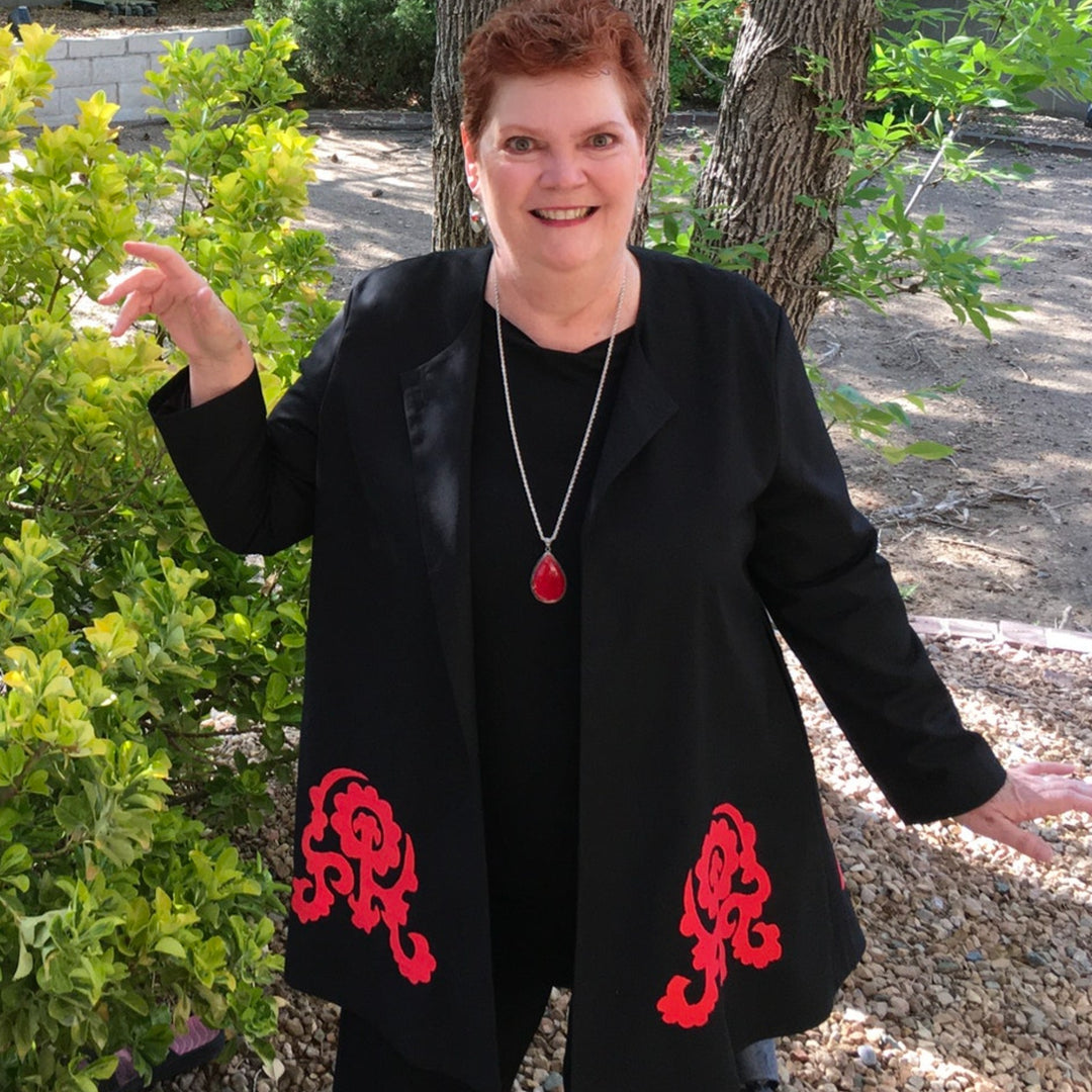 Front view of black swing jacket with large red hand-embroidered patterns, on model